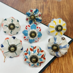 Peut inclure: Sept boutons de tiroir en céramique en forme de fleur festonnée. Chaque bouton présente une base blanche avec des motifs peints à la main en bleu, rouge, jaune et vert, centrés par une fixation en métal de couleur laiton antique.