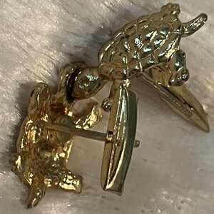 May include: Gold-toned cufflinks featuring a turtle design. The cufflinks have a textured surface and a classic post closure. The turtle is detailed with a shell pattern and raised features. The jewelry is set against a soft, white background.