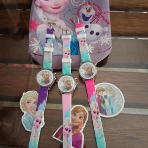 May include: Three children's watches with colourful straps featuring characters from the animated film "Frozen." The watch faces display the characters, and the straps are purple, pink, and teal. A matching bag is in the background.