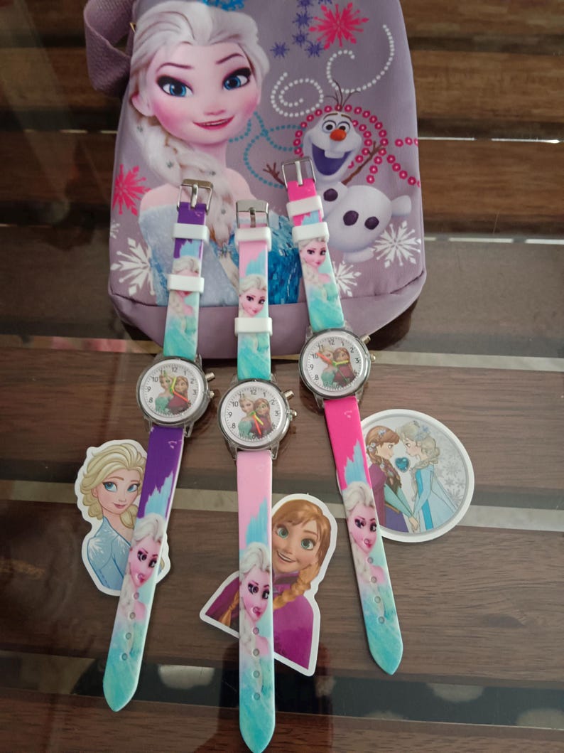 May include: Three children's watches with colourful straps featuring characters from the animated film "Frozen." The watch faces display the characters, and the straps are purple, pink, and teal. A matching bag is in the background.