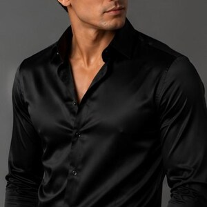May include: A long-sleeved black button-down shirt with a smooth, satin-like finish. The shirt features a classic collar, a front button placket with matching black buttons, and fitted cuffs. The fabric has a subtle sheen that reflects light.