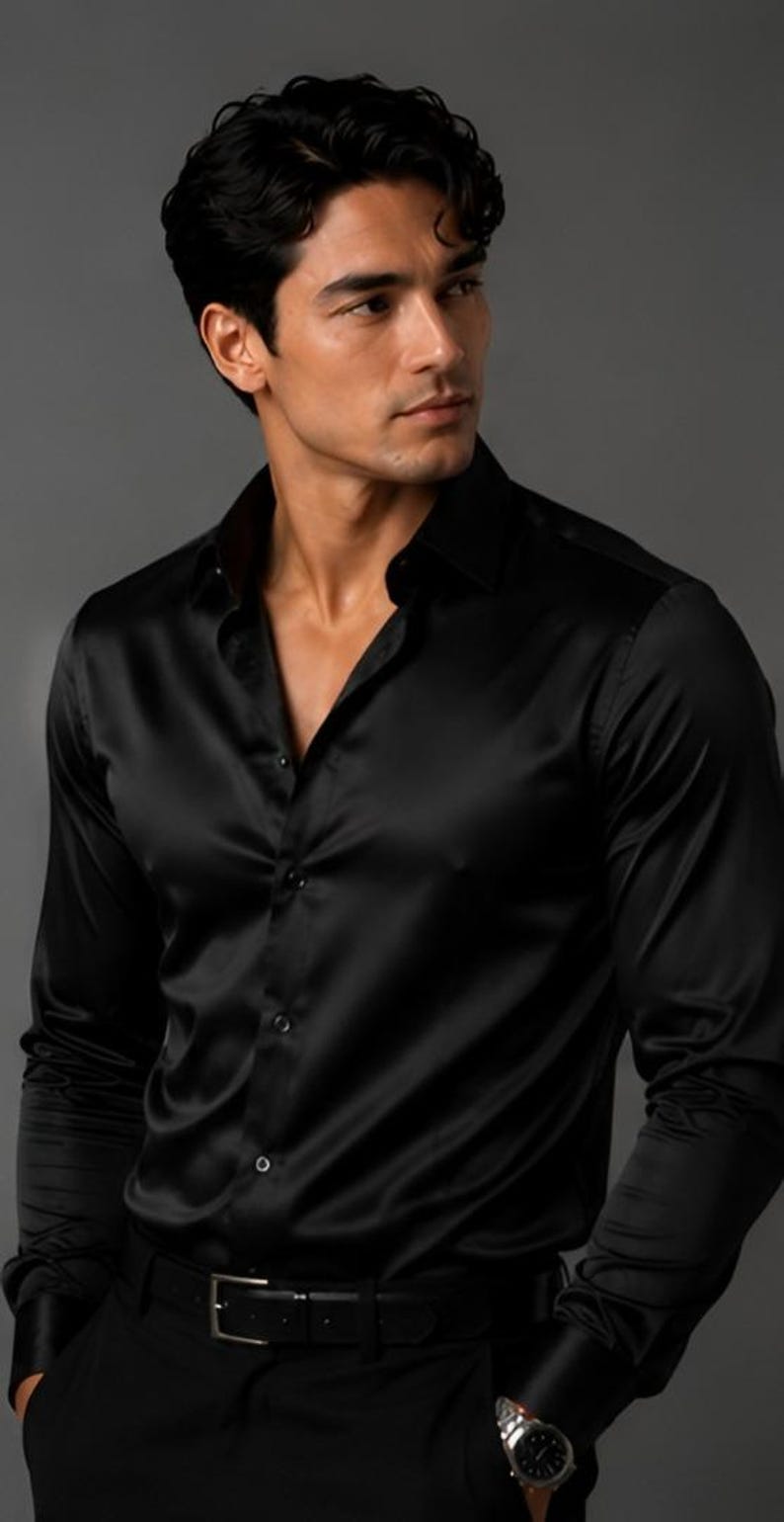 May include: A long-sleeved black button-down shirt with a smooth, satin-like finish. The shirt features a classic collar, a front button placket with matching black buttons, and fitted cuffs. The fabric has a subtle sheen that reflects light.