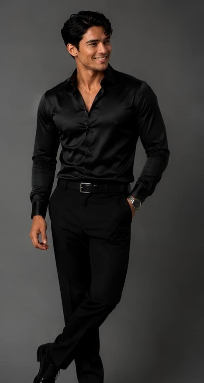 May include: A long-sleeved black button-down shirt with a smooth, satin-like finish, paired with matching black trousers and a black leather belt. The shirt features a classic collar, buttoned cuffs, and a front button placket, creating a monochromatic look.
