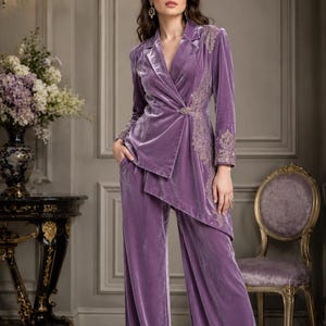 Könnte beinhalten: Ein lavendelfarbener Hosenanzug aus Samt mit einem Wickelblazer mit aufwendigen Stickereien an Ärmel und Revers. Die weite Hose und der Blazer haben einen passenden Lilaton. Ein klassisches und elegantes Ensemble.