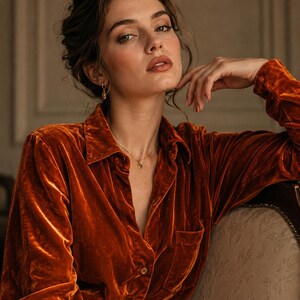 Op de afbeelding: Een overhemd met lange mouwen en knoopsluiting, gemaakt van fluweelachtige stof in de kleur gebrand oranje. Het overhemd heeft een klassieke kraag, een enkele borstzak aan de linkerkant en bijpassende knopen langs de voorzijde met textuur.