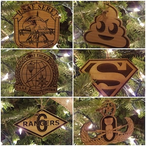 May include: Five wooden Christmas ornaments with different designs. The ornaments are all brown and feature various military and pop culture themes. The ornaments include a US Air Force emblem, a Superman logo, a poop emoji, a Rangers logo, and a bomb with wings.