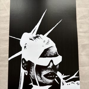 Könnte beinhalten: Schwarz-Weiß-Kunstdruck mit einem stilisierten Porträt. Das Bild zeigt eine Person mit Sonnenbrille und Kopfbedeckung mit scharfen, spitzen Elementen. Das Kunstwerk hat einen kontrastreichen, grafischen Stil.