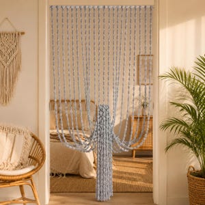 May include: A light gray beaded string curtain featuring multiple vertical strands of small, uniform oval-shaped beads. The curtain is suspended from a horizontal rod across a doorway, with the center section gathered and tied together.