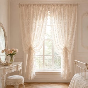 Könnte beinhalten: Ein Paar bodenlange, cremefarbene Spitzengardinen, die an einer Stange vor einem Fenster hängen. Die Vorhänge weisen ein kompliziertes Blumenmuster auf und sind an den Seiten gerafft, wodurch Licht durch den halbtransparenten Stoff in den Raum fällt.