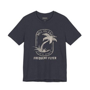 May include: A dark heather navy blue short-sleeve t-shirt with a distressed graphic print. The design features a palm tree inside an oval border with the text NULL ISLAND 0°00'N 0°00'E and the words FREQUENT FLYER printed below the graphic.