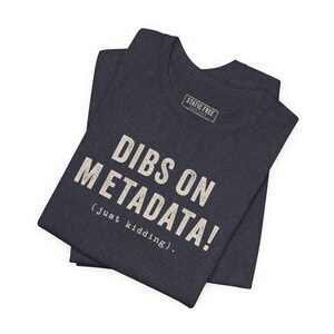 May include: A dark charcoal heather crew neck t-shirt featuring the off-white text DIBS ON METADATA! (just kidding). A small rectangular label on the inside collar reads STATIC FREE. The fabric has a visible heathered texture throughout the garment.