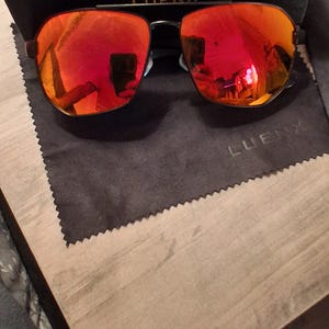 May include: Sunglasses with reflective red lenses and a black frame, presented with a black box and a cleaning cloth. The box has the text "SEE BETTER WORLD" and the brand name "LUENX".