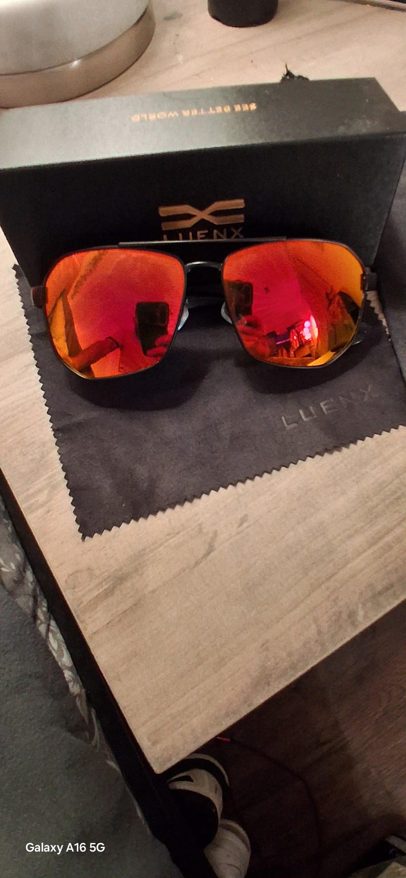 May include: Sunglasses with reflective red lenses and a black frame, presented with a black box and a cleaning cloth. The box has the text "SEE BETTER WORLD" and the brand name "LUENX".