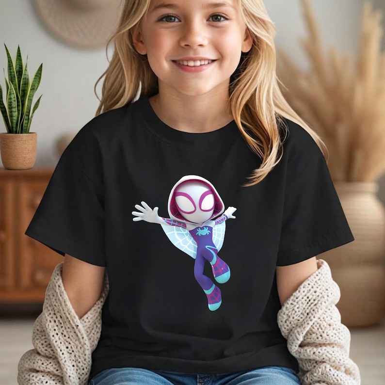 May include: Black t-shirt featuring a cartoon illustration of Spider-Gwen in a dynamic pose. The character is depicted in a white hooded mask, purple and blue suit, and web wings. The shirt is worn by a young girl.