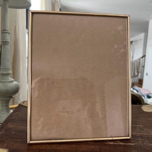 May include: A gold-colored picture frame with a light brown mat. The frame is empty and ready for a photo.
