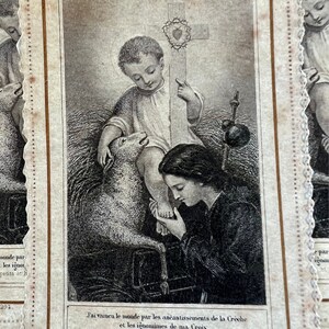 May include: A black and white illustration of a religious scene. A young boy sits with a lamb at his feet, holding a cross with a crown of thorns. A woman kneels before him, looking up at him. The text reads "LA DIVINE ROYAUTE DE JESUS. et son Signe." and "J'ai vaincu le monde par les an&eacute;antissements de la Cr&egrave;che et les ignominies de ma Croix. R&eacute;jouisses-vous, petits et humbles, car vous vaincres avec Moi."