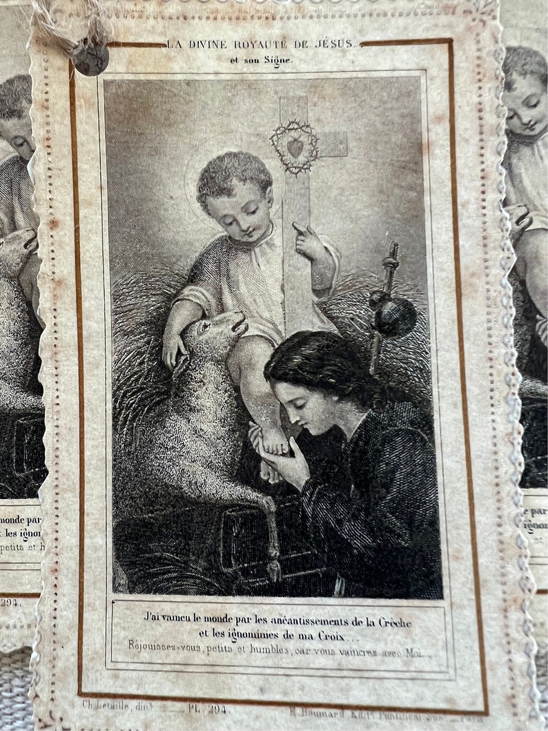 May include: A black and white illustration of a religious scene. A young boy sits with a lamb at his feet, holding a cross with a crown of thorns. A woman kneels before him, looking up at him. The text reads "LA DIVINE ROYAUTE DE JESUS. et son Signe." and "J'ai vaincu le monde par les an&eacute;antissements de la Cr&egrave;che et les ignominies de ma Croix. R&eacute;jouisses-vous, petits et humbles, car vous vaincres avec Moi."