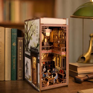 May include: A wooden book nook diorama featuring a two-story traditional Chinese interior scene with miniature furniture, figures, and warm lighting. The exterior side panel displays a printed illustration of a tree and Chinese text, 青瓦迷云.