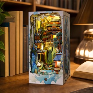 Peut inclure: Un insert de bibliothèque rectangulaire en bois présentant un diorama 3D multicouche d'un paysage traditionnel d'Asie de l'Est avec des pagodes, des ponts et des falaises rocheuses. La scène est éclairée de l'intérieur, révélant des tons bleus, verts et dorés.
