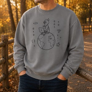Könnte beinhalten: Ein grauer Rundhals-Pullover mit einer schwarzen Strichgrafik, die einen Außerirdischen zeigt, der auf einem Globus sitzt und einen Laptop benutzt. Das Design umfasst Binärcode, ein WLAN-Symbol, geschweifte Klammern und ein kleines Käfer-Symbol.