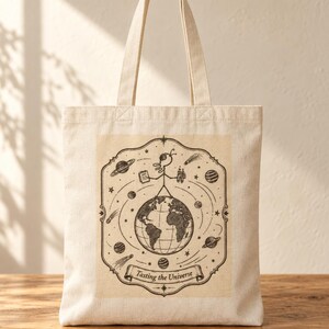 Peut inclure: Un sac fourre-tout en toile beige orné d'une illustration à l'encre noire représentant un personnage filiforme debout sur la Terre, entouré de planètes, d'étoiles et de comètes. Le motif est encadré par une bordure avec la mention Tasting the Universe.