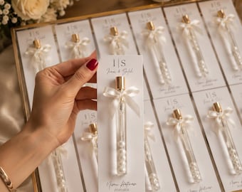 May include: A collection of clear glass tubes filled with white pearls, each attached to a white card featuring the text I|S Irem & Salih and Nisan Hatirasi 25/07/2026. Each tube is topped with a gold cap and a small white satin ribbon bow.