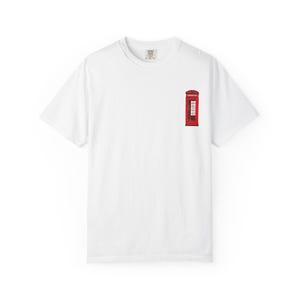 May include: A white short-sleeve t-shirt featuring a small graphic on the left chest area. The graphic depicts a classic red British telephone box with black detailing. The shirt has a crew neckline and a standard fit, made of solid white fabric.