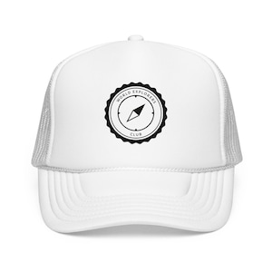 May include: White trucker cap with a curved peak and mesh back. The front displays a black circular emblem with the words "WORLD EXPLORERS CLUB" and a compass design. A practical accessory for explorers.