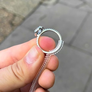 May include: A silver-toned ring featuring a round, clear faceted stone set in a prong setting. A clear, coiled plastic ring size adjuster is wrapped around the bottom portion of the metal band to reduce the inner diameter for a tighter fit.