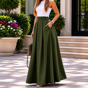Op de afbeelding: Een olijfgroene rok met hoge taille en een lengte tot op de grond, voorzien van diepe plooien en zijzakken, gecombineerd met een mouwloze witte top met ronde hals. De rok heeft een gestructureerde tailleband en een wijde, vloeiende snit.