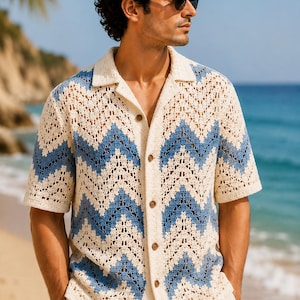 May include: A short-sleeve button-down shirt featuring an open-knit crochet construction with a cream and blue chevron pattern. The garment has a classic collar, a straight hem, and five visible brown buttons running down the center front.