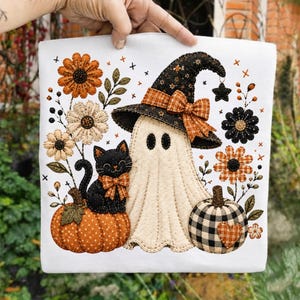 May include: A white fabric panel featuring an embroidered design of a cream-colored ghost wearing a black witch hat with an orange plaid bow, a black cat with an orange plaid bow sitting on an orange polka dot pumpkin, and a black and white buffalo check pumpkin.