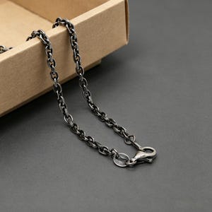 May include: A dark silver-toned metal chain necklace featuring rounded oval links with a polished finish. The chain includes a secure lobster claw clasp mechanism at one end, designed for fastening the necklace around the neck.