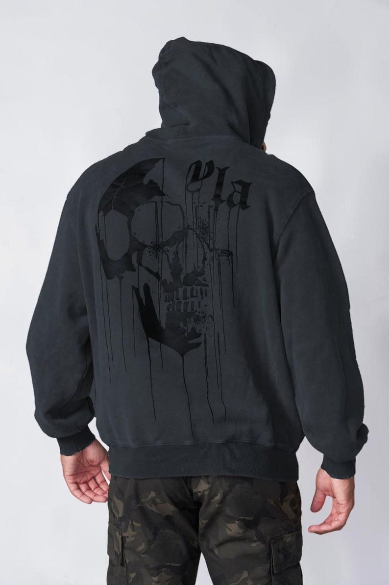 Puede incluir: Una sudadera con capucha negra que presenta un gr&aacute;fico grande de una calavera oscura y goteante impreso en la espalda. El dise&ntilde;o incluye letras estilizadas sobre la calavera. La sudadera tiene mangas largas con pu&ntilde;os y dobladillo acanalados.