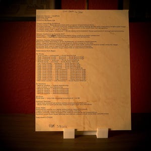 May include: A vintage document, likely a report, is propped up on a white stand. The paper has aged to a warm, yellowish hue, with handwritten notes and typed text. The document is set against a dark background with a red wall.