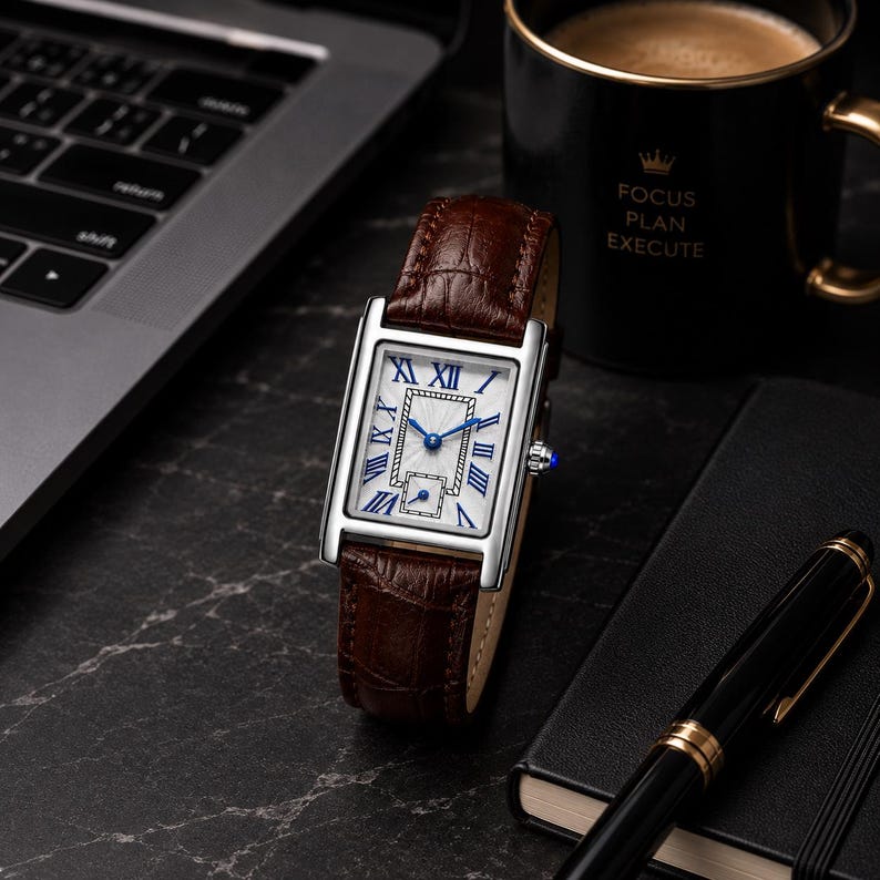 May include: A rectangular wristwatch with a silver-tone case, a white dial featuring blue Roman numeral hour markers, and a brown crocodile-embossed leather strap. The watch has blue hands and a small sub-dial at the bottom of the face.