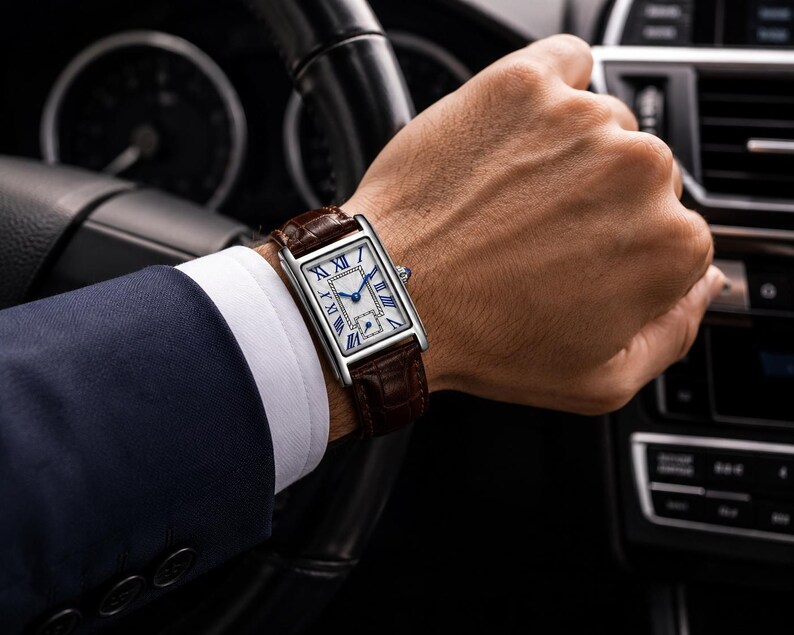 May include: A rectangular wristwatch with a silver-tone case, a white dial featuring black Roman numerals, and blue hands. The watch is secured with a dark brown textured leather strap with a visible grain pattern and a polished metal buckle.