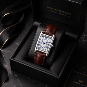 May include: A rectangular wristwatch with a silver-tone case, a white dial featuring blue Roman numerals, and a brown crocodile-embossed leather strap. The watch is presented in a black box labeled "TIMELESS ELEGANCE PRECISION BY DESIGN."