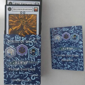 Op de afbeelding: Een trading card game set met een blauwe doos met de tekst "VALKYRIE TRADING CARD GAME" en "GENESIS OF WRATH". De doos bevat kaarten met karakterillustraties. Een regelboek is ook inbegrepen.