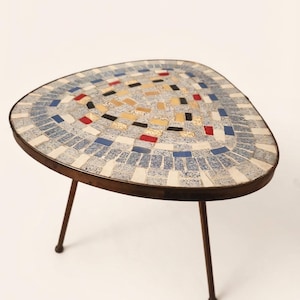 May include: A triangular side table with a mosaic top featuring small rectangular tiles in shades of blue, white, red, yellow, and black. The tabletop is framed by a thin metal edge and supported by three slender, dark brown metal legs.