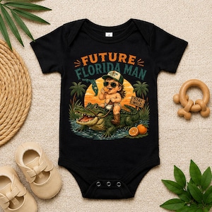May include: Black baby bodysuit with a graphic of a baby riding an alligator, wearing sunglasses and a hat. The text reads "FUTURE FLORIDA MAN" and "STAY WILD". Oranges and palm trees are also featured in the design.