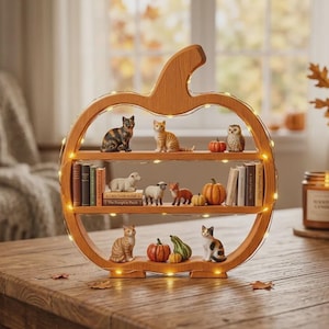 Pode incluir: Uma prateleira de madeira em forma de abóbora com três níveis, iluminada por luzes integradas. As prateleiras contêm figuras de animais em miniatura, incluindo gatos, ovelhas e uma coruja, além de pequenas abóboras, cabaças e livros.