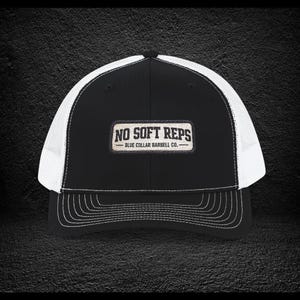 May include: Black and white trucker hat with the text "NO SOFT REPS" on a rectangular patch. The hat features a black front panel, a white mesh back, and a curved brim with white stitching. The text "BLUE COLLAR BARBELL CO." is below the main text.
