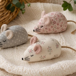 May include: Three stuffed fabric mice toys featuring soft textures and embroidered details. One mouse is grey with white polka dots, while the other two are cream and pink with delicate floral patterns. Each mouse has small ears and a jute rope tail.