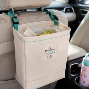 Könnte beinhalten: Beige Auto-Organizer-Tasche mit türkisfarbenen Nähten und Riemen, die an einer Kopfstütze befestigt ist. Die Tasche hat eine rechteckige Form mit einem Etikett "The Practical Stitcher". Eine rosa-blaue Wasserflasche befindet sich im Getränkehalter.