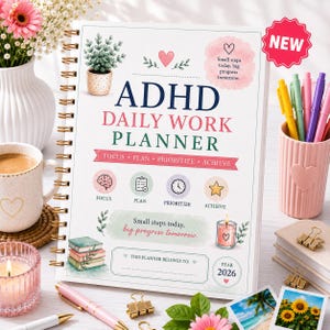 Puede incluir: Una agenda diaria ADHD 2026 de espiral con una cubierta blanca que presenta texto, una planta en maceta e iconos para enfocar, planificar, priorizar y lograr. La cubierta incluye la frase Small steps today, big progress tomorrow y un corazón.