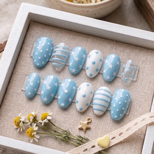 May include: A set of twelve oval-shaped press-on nails featuring a light blue and white color palette. The designs include white polka dots on blue, blue polka dots on white, blue and white horizontal stripes, and white stars on blue backgrounds.
