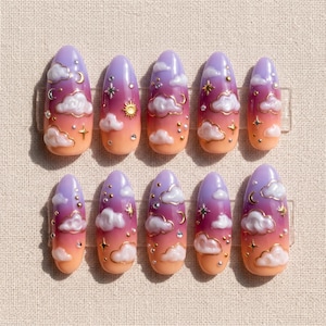 May include: A set of ten almond-shaped press-on nails. Each nail features a gradient design of orange, pink, and purple, with white cloud accents, gold stars, and small gems. The nails are designed to resemble a sunset sky.