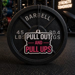 May include: A black barbell weight plate with the word "BARBELL" in white. The plate weighs 20.4 kg (45 lbs). A sticker with the text "PULL OUT" and "PULL UPS" is attached. The background includes gym equipment and the neon sign "DISCIPLINE TODAY STRENGTH TOMORROW".