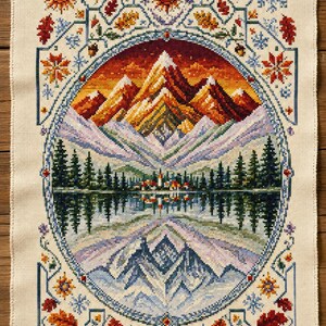 Puede incluir: Un bordado de punto de cruz rectangular sobre tela color crema con un marco ovalado central. El diseño muestra un paisaje montañoso con atardecer, bosque, lago y el reflejo de las montañas. Motivos estacionales como soles, copos de nieve y hojas bordean el marco.